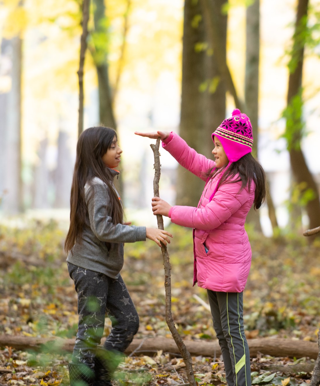 Two young girls measure how high a stick is with their hands for use in shelter building.