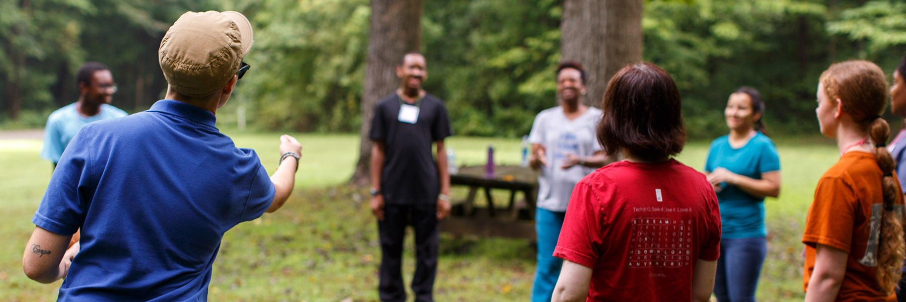 A Bradford Woods facilitator guides a smiling group in an activity in an outdoor green space.
